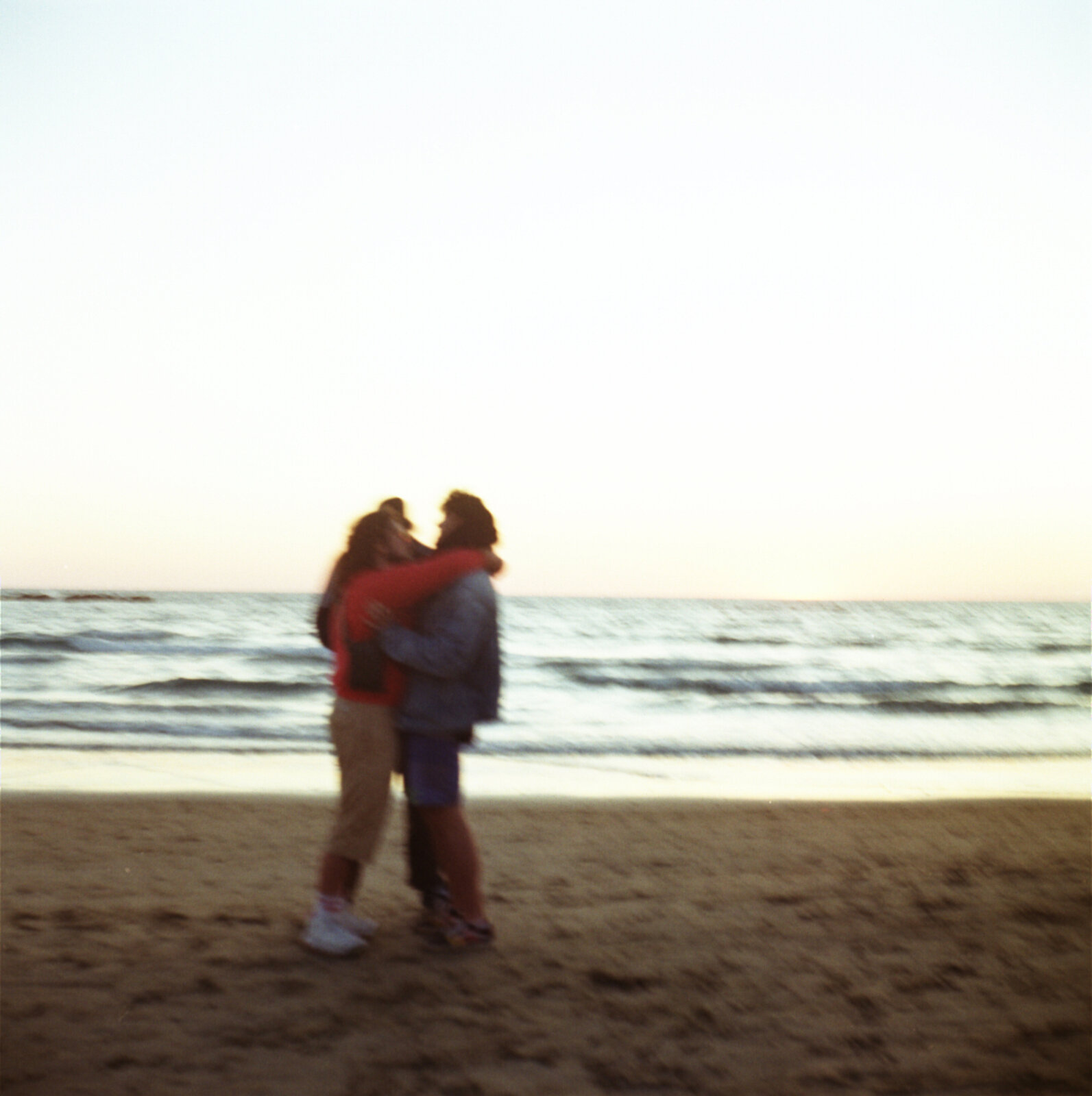 Two people silhouetted, embracing on a beach at dusk