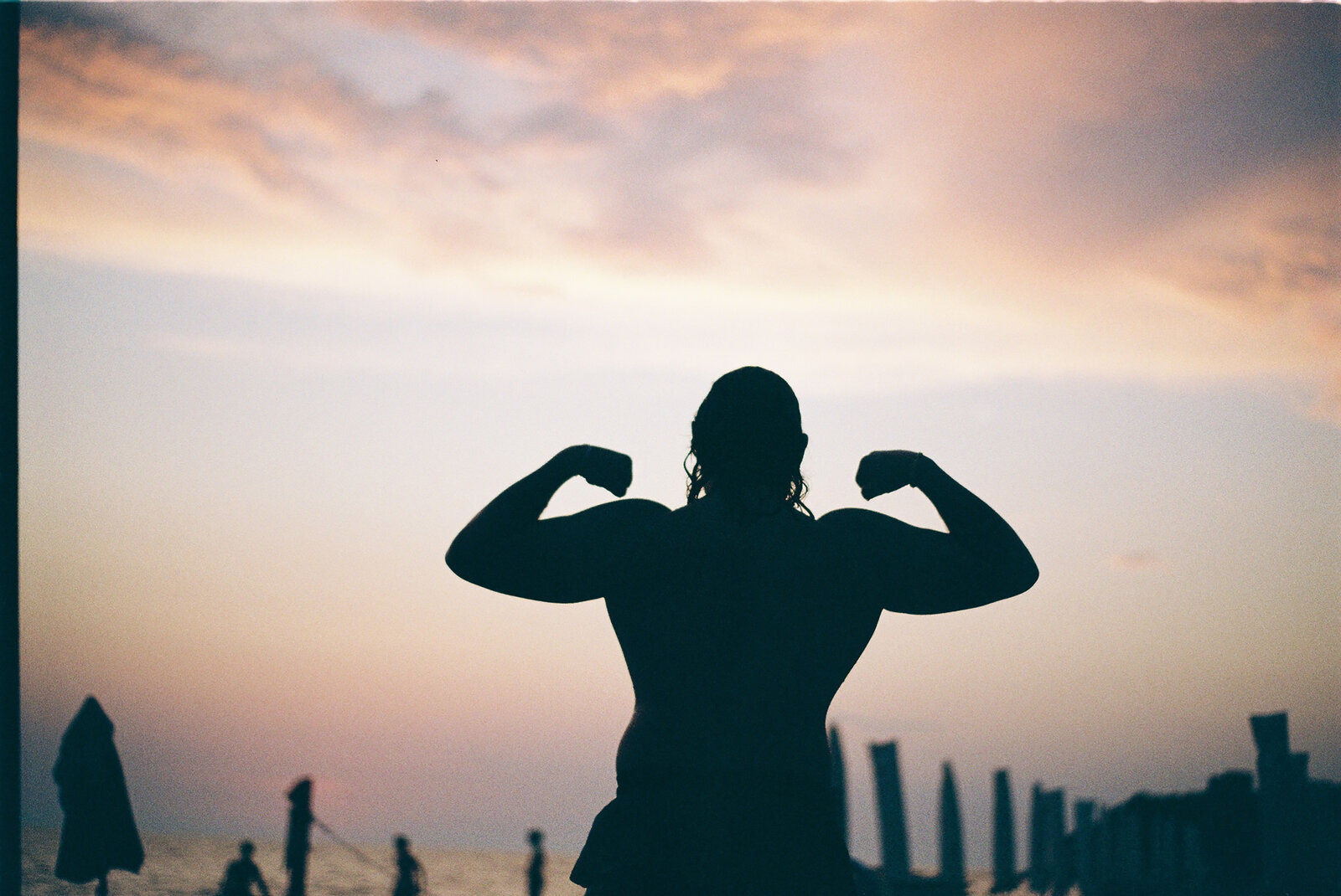 A silhouette flexing against a vivid orange sunset over the sea