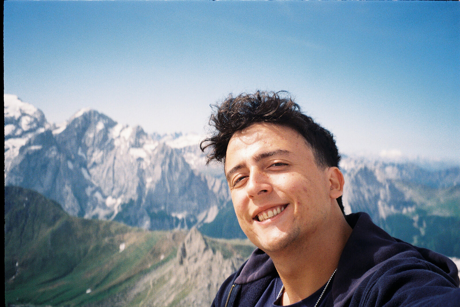 Matteo smiling on a mountain ridge, snow-capped peaks behind him